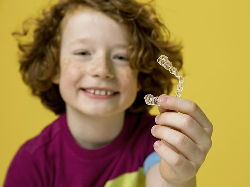 child holding an aligner for web article on children's teeth and braces